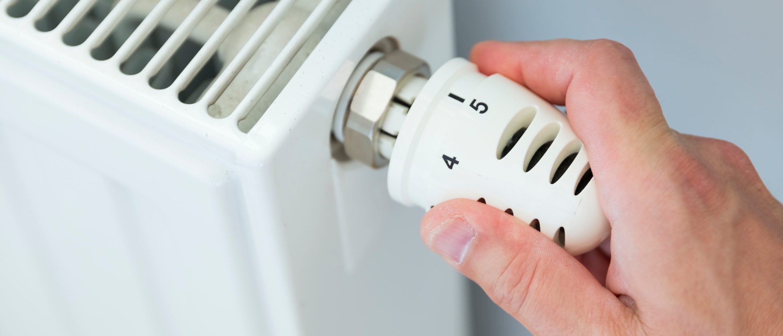 hand,adjusting,thermostat,valve,of,heating,radiator,in,a,room.